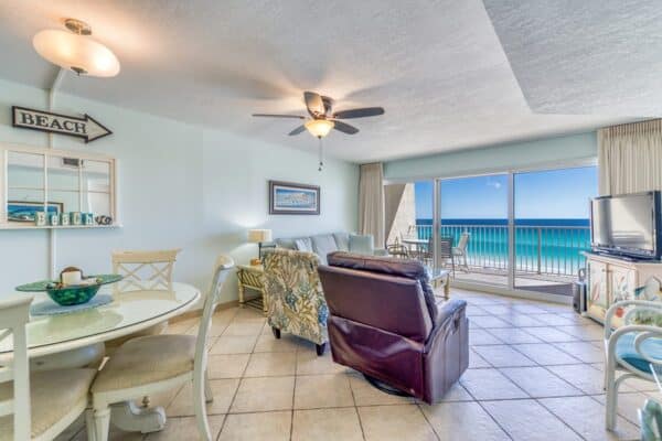 The B405 living room has ocean views, a dining area, ceiling fan, cozy seating with TV and armchairs, and a balcony.