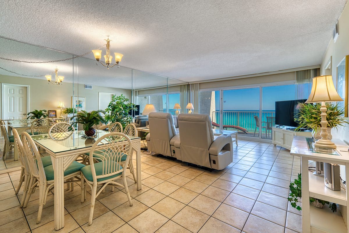 Bright living and dining area at the condominium with tiled floors, glass table, recliners, TV, big windows, and ocean view.