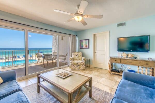 Living room in condo C204 at The Beach House with balcony ocean view, furnished with sofa, armchair, and HDTV.