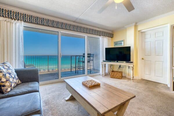Living room with sofa, coffee table, TV, and sliding doors to a balcony overlooking the ocean at the condominium complex.