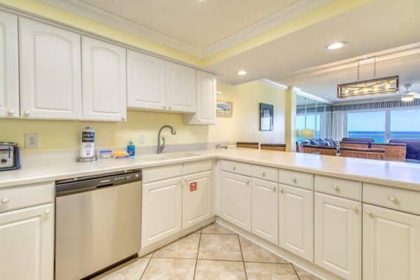 Bright kitchen with white cabinets, modern appliances, and tile floor at The Beach House Condominiums.