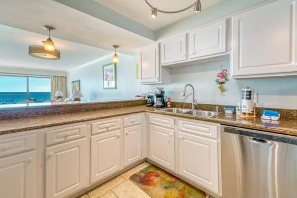 Modern kitchen with white cabinets, granite countertops, and stainless steel dishwasher. Coffee maker on counter near large window.