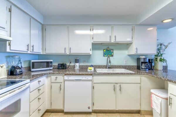 A kitchen with white cabinets, granite countertops, and standard appliances including a microwave, blender, toaster, coffee maker, and dishwasher.