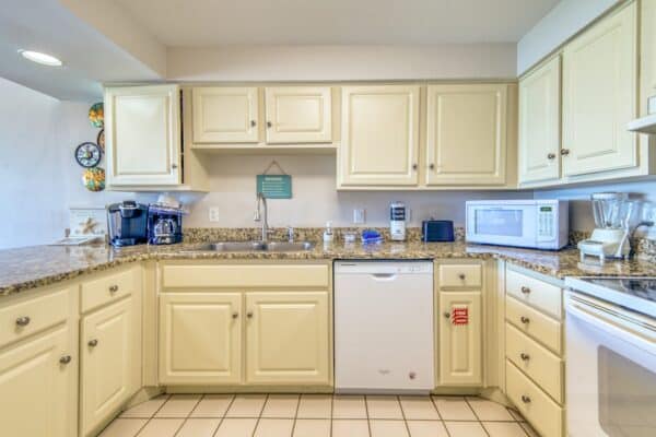 A kitchen with beige cabinets, granite countertops, a sink, a dishwasher, a coffee maker, and various small appliances.