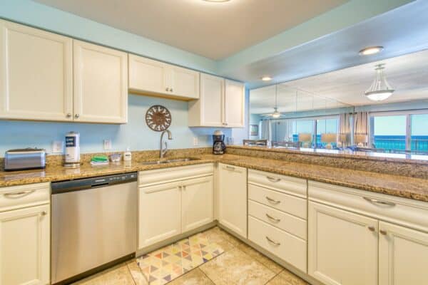 Bright kitchen at the Beach House Condominiums with white cabinets, granite tops, and ocean view via large windows.