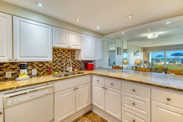 Modern kitchen with white cabinets and granite countertops; open dining area, large windows, outdoor view at the condos.