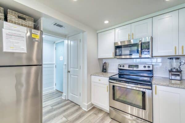 Modern kitchen with stainless steel appliances, white cabinets, light wood flooring, and a countertop. Refrigerator on the left.