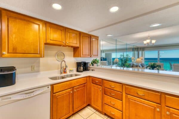 Kitchen with wooden cabinets, white counters, double sink, dishwasher, coffee maker, and mirrored wall reflecting ocean view.