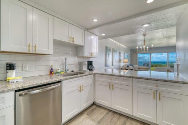 L-shaped kitchen with white cabinets, granite counters, and stainless appliances, opening to a living room with an ocean view.