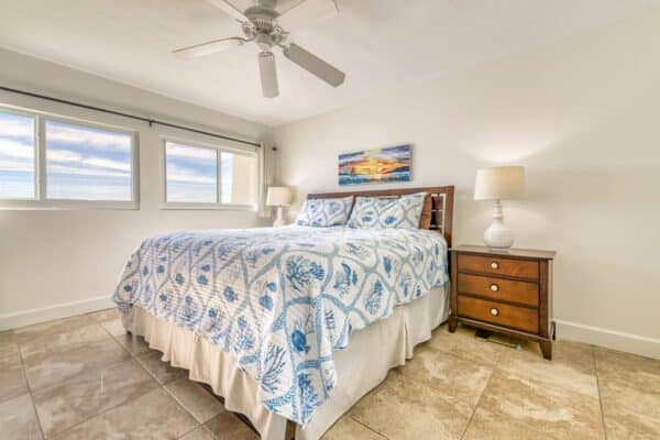 Bedroom with a large bed covered in a blue and white quilt, wooden nightstands with lamps, and a ceiling fan above.