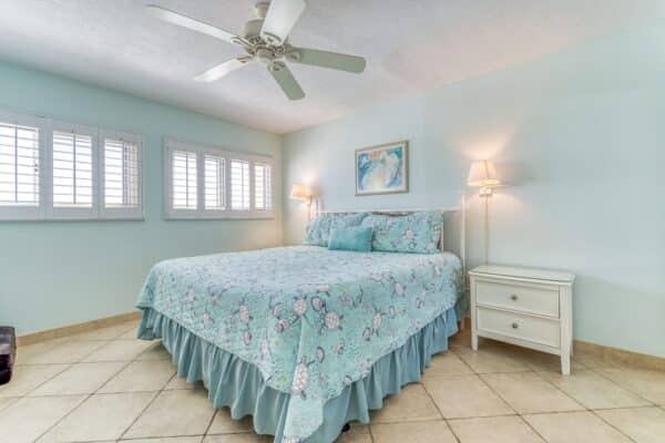 A bedroom with a floral bedspread, two nightstands with lamps, a ceiling fan, tiled floor, and a painting above the bed in B405.