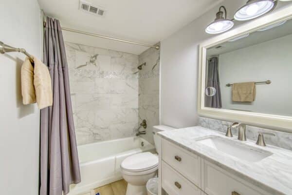 Modern bathroom in Beach House Condominium with marble tiles, combo tub/shower, vanity with C103 sink, mirror and towel rack.