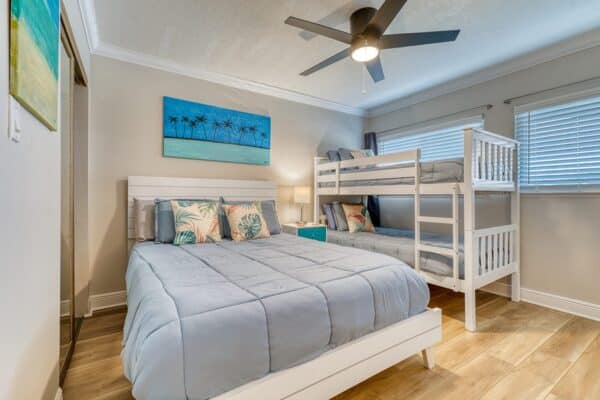 Bedroom at The Beach House Condominiums with double bed, bunk bed, wood floors, ceiling fan, blue accents, beach art.