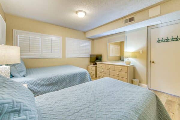 Bright bedroom with twin beds, light blue bedding, a dresser, TV and beige walls at Beach House Condos (D104).