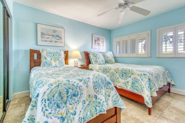 Brightly lit room in Beach House Condominiums with two twin beds, blue floral bedding, wooden headboards and beach-themed decor.