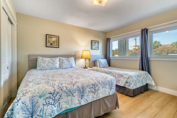 Bedroom at the condominium with a queen and twin bed, blue and white bedding, a lamp, and two windows with dark curtains.