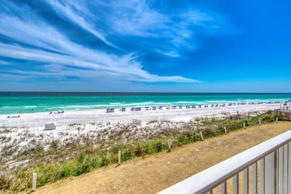 A203 view at Beach House Condominiums: beachfront balcony overlook of sandy beach, colorful umbrellas, turquoise waters under a cloudy sky.