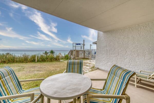 Balcony at Beach House Condos with striped chairs, overlooking a beach under clear skies.