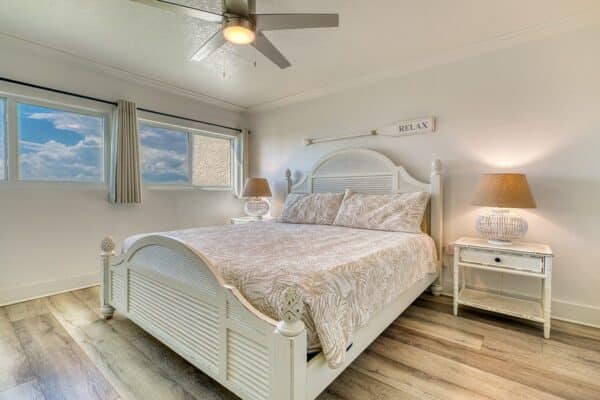 Bedroom at The Beach House Condominiums featuring a white bed, two nightstands, and a wall-mounted oar labeled “RELAX.”