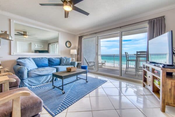 Bright living room at Beach House Condos with blue sofa, wooden furniture, and balcony A203 showcasing the ocean view.