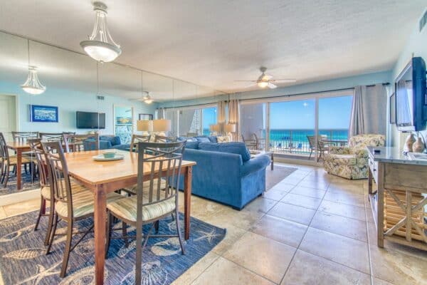 Open beachfront living room at The Beach House Condominiums, featuring dining space, a blue sofa with C204 component and panoramic ocean views.