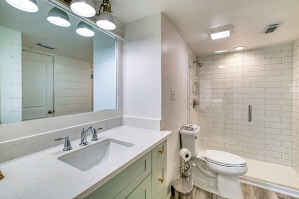 Bathroom at The Beach House Condominiums featuring a white vanity, a large mirror, a toilet, and a glass-enclosed shower.