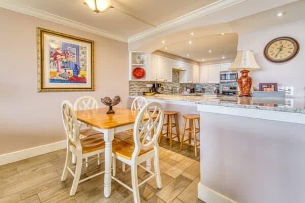 Modern kitchen and dining area with latest appliances, wooden table, white chairs and colorful wall art at Beach House Condominiums.