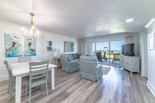 B105-themed living room with coastal decor and dining area at the Beach House Condominiums, leading to outdoors.