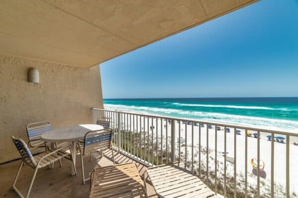 Balcony view at Beach House Condominiums, showcasing sandy beach and clear blue ocean under bright sky.