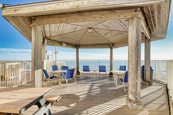Covered wooden patio area with blue chairs at Beach House Condominiums, offering a shaded ocean view.