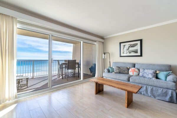 Living room with a sofa and sliding doors leading to an ocean-view balcony at The Beach House Condominiums.