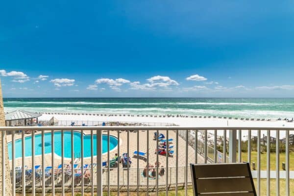 Balcony view at The Beach House Condos with a pool and ocean under a blue sky with clouds.