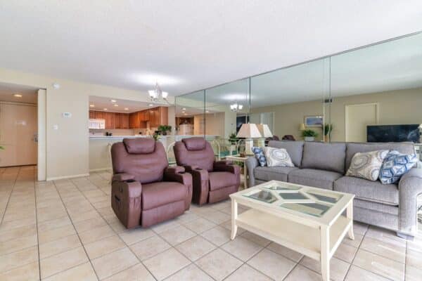 Spacious living room with grey couch, two recliners and open-concept kitchen at The Beach House Condominiums.