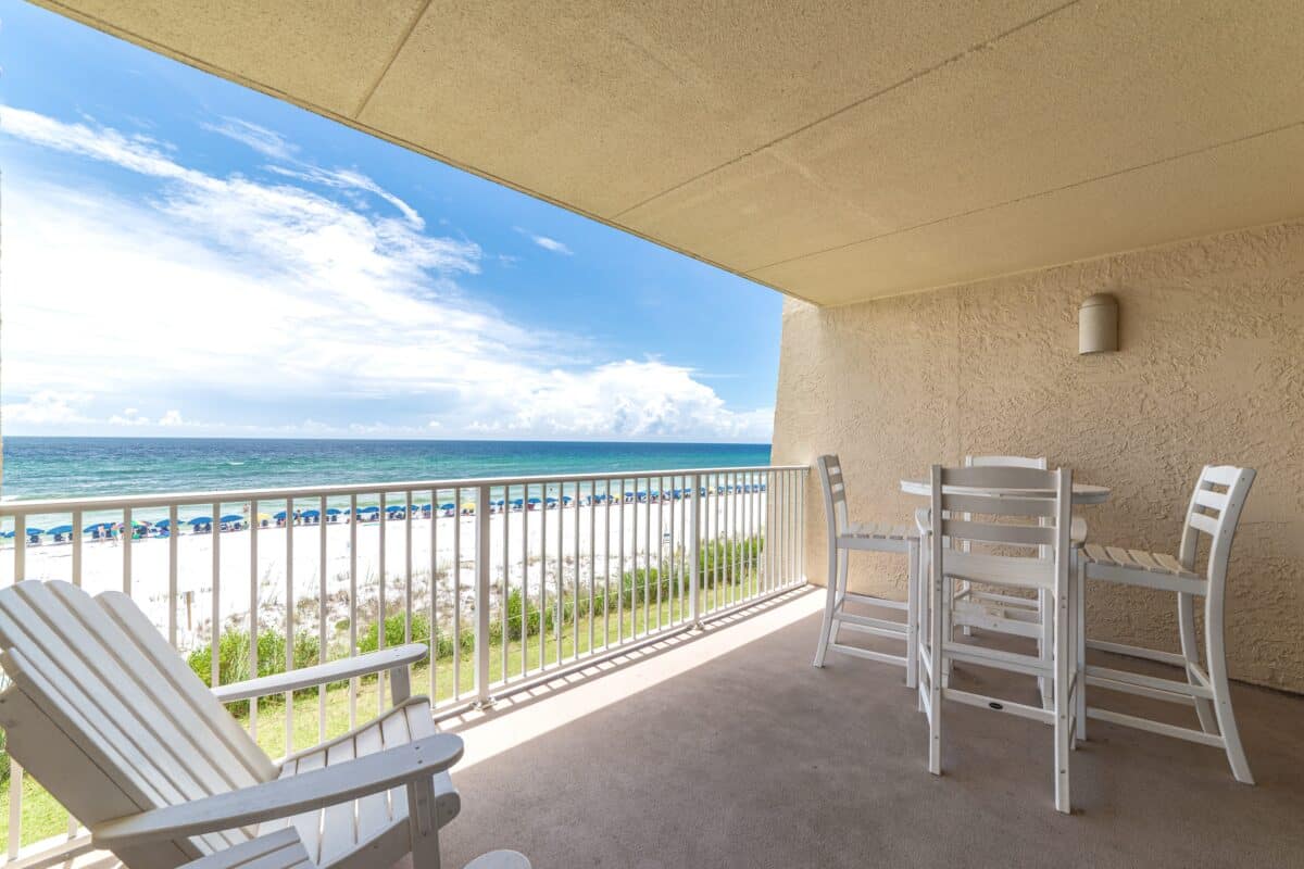 A private balcony at Beach House Condominiums furnished with white chairs overlooking the Gulf's shoreline.