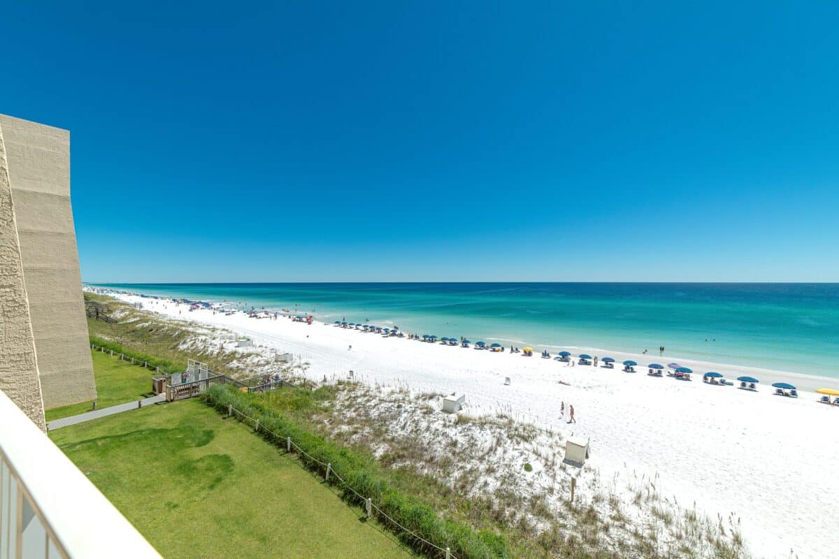View from the side of Beach House Condominiums overlooking the crowded white sandy beach and clear blue Gulf waters.