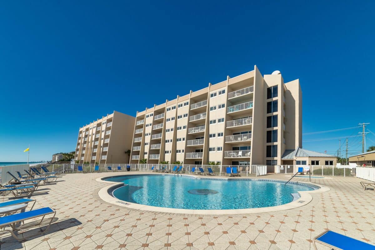 Modern beachfront condos at The Beach House Condominiums with a pool and lounge chairs under a blue sky.