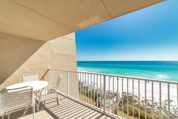 Oceanfront balcony view at Beach House Condos with seating overlooking a sandy beach and blue waters.