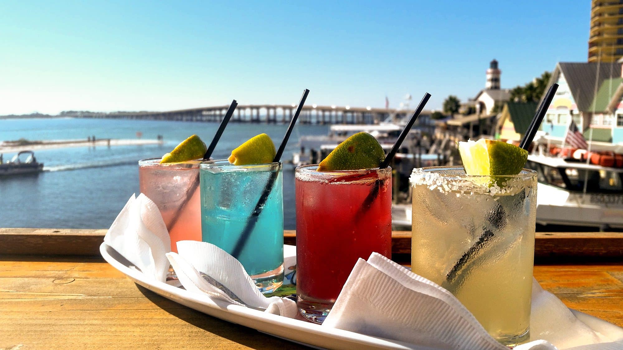 Colorful cocktails with lime on tray at The Beach House Condominiums, lighthouse in backdrop.