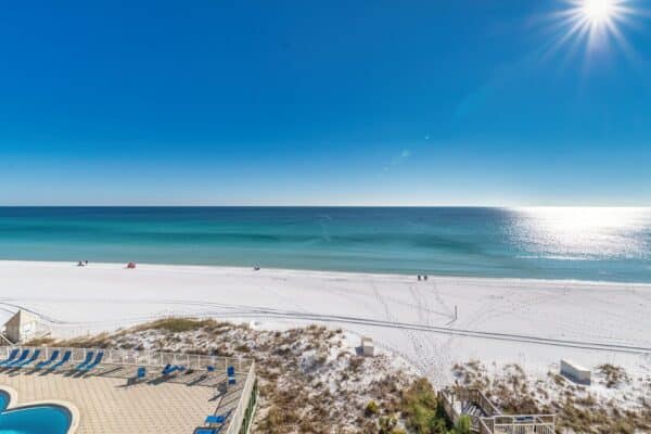 Sunny beach view with clear water and white sand, C602 Condo from The Beach House in focus.