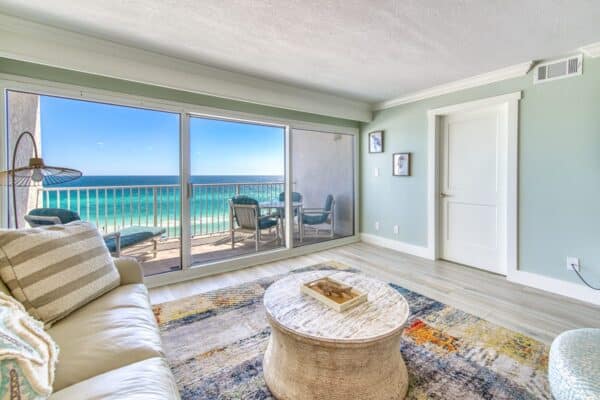 Ocean view from living room with large windows in The Beach House Condominiums. Includes sofa, coffee table, and balcony seating.