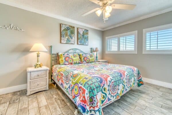 Bright, colorful bedroom B502 at The Beach House Condominiums featuring a patterned bedspread, wicker furniture and tropical decor.