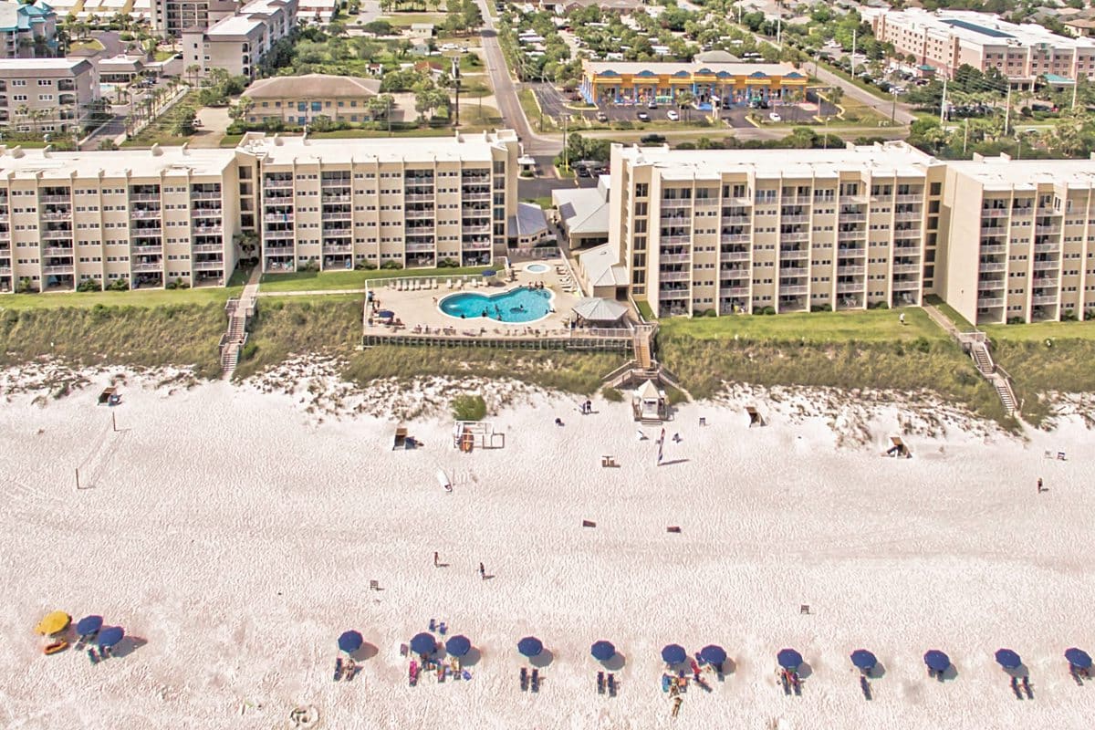 Aerial view of Beach House Condominiums with vibrant umbrellas on white sand and neighboring structures.