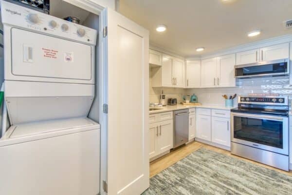 A modern kitchen with white cabinets, stainless steel appliances, and a stackable washer and dryer in an open closet.